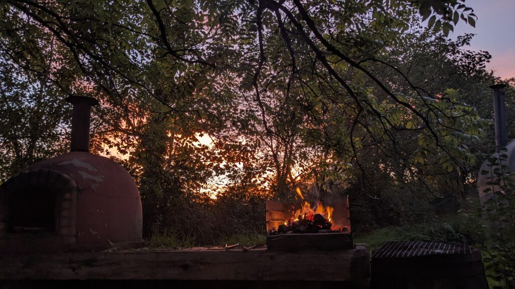 A fire burning in front of a stunning sunset seen through leafy trees